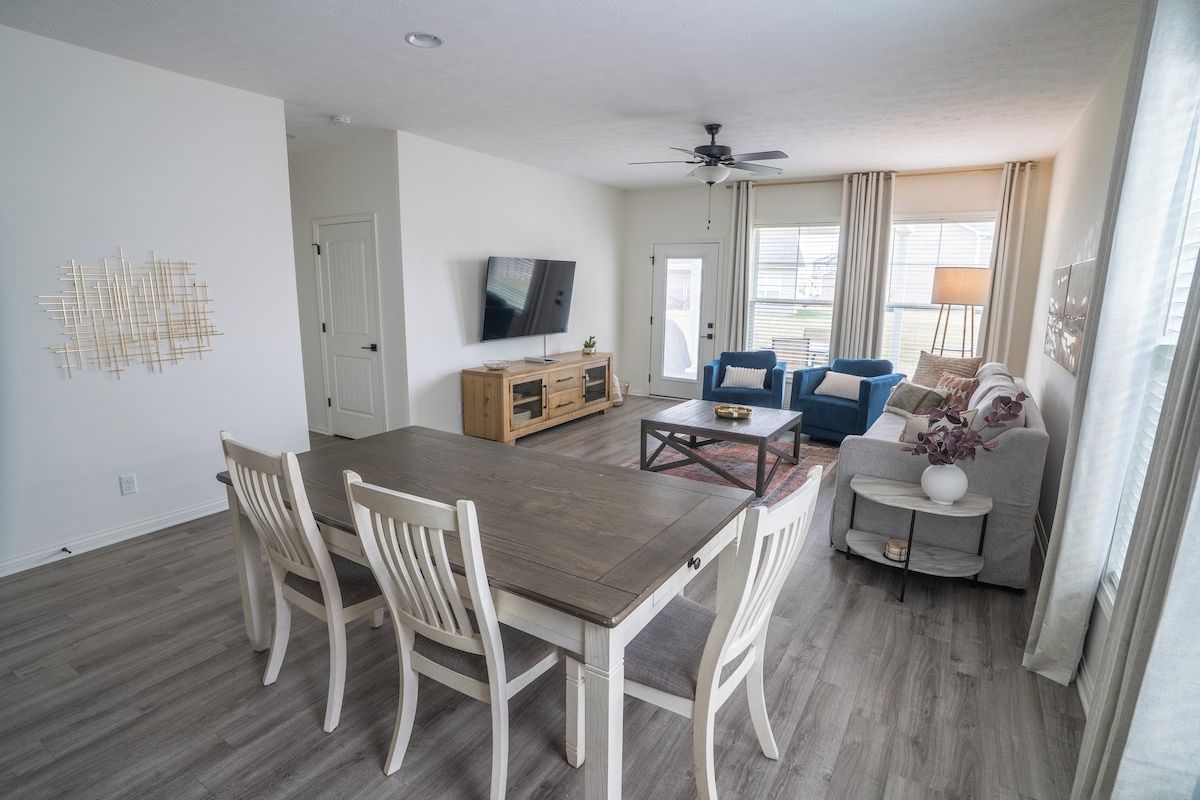 A modern living room with a dining table, chairs, a sofa, and a television.