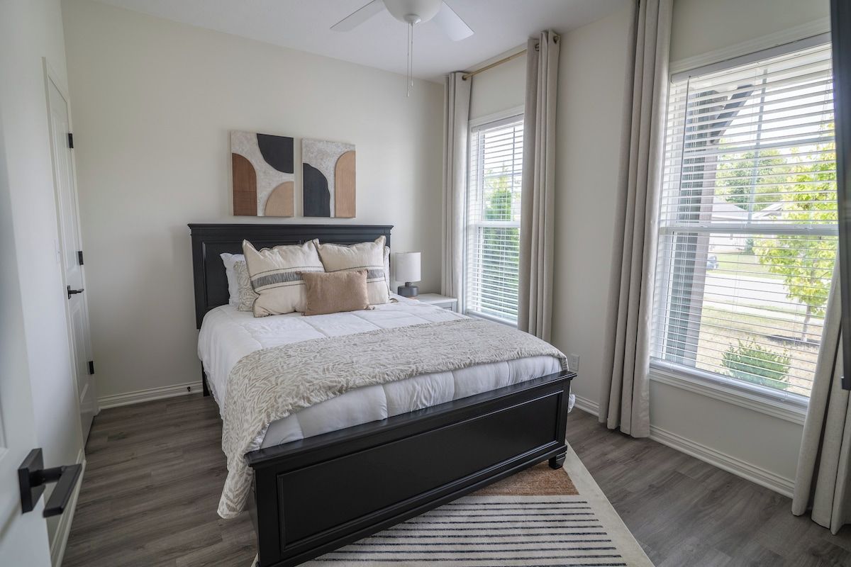 A bedroom with a bed, a ceiling fan, a window with blinds, and a door.