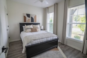 A bedroom with a bed, a ceiling fan, a window with blinds, and a door. - Bluegrass Nest- Sleeps 8 (Owensboro)