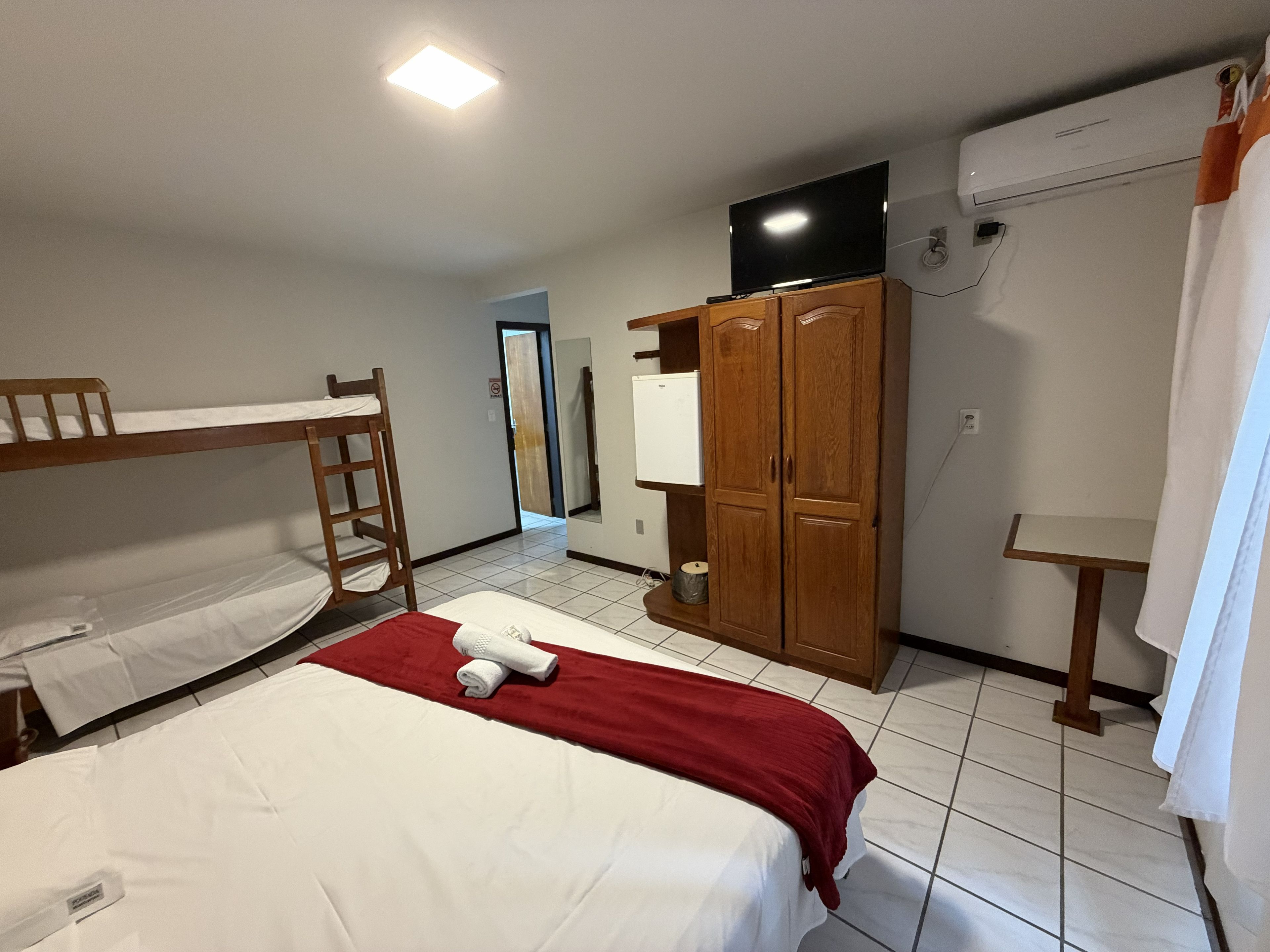 Habitación de hotel con literas, armario de madera, televisor de pantalla plana y equipo de aire acondicionado.
