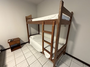 A bunk bed with a wooden frame and white bedding in a room with tiled flooring.