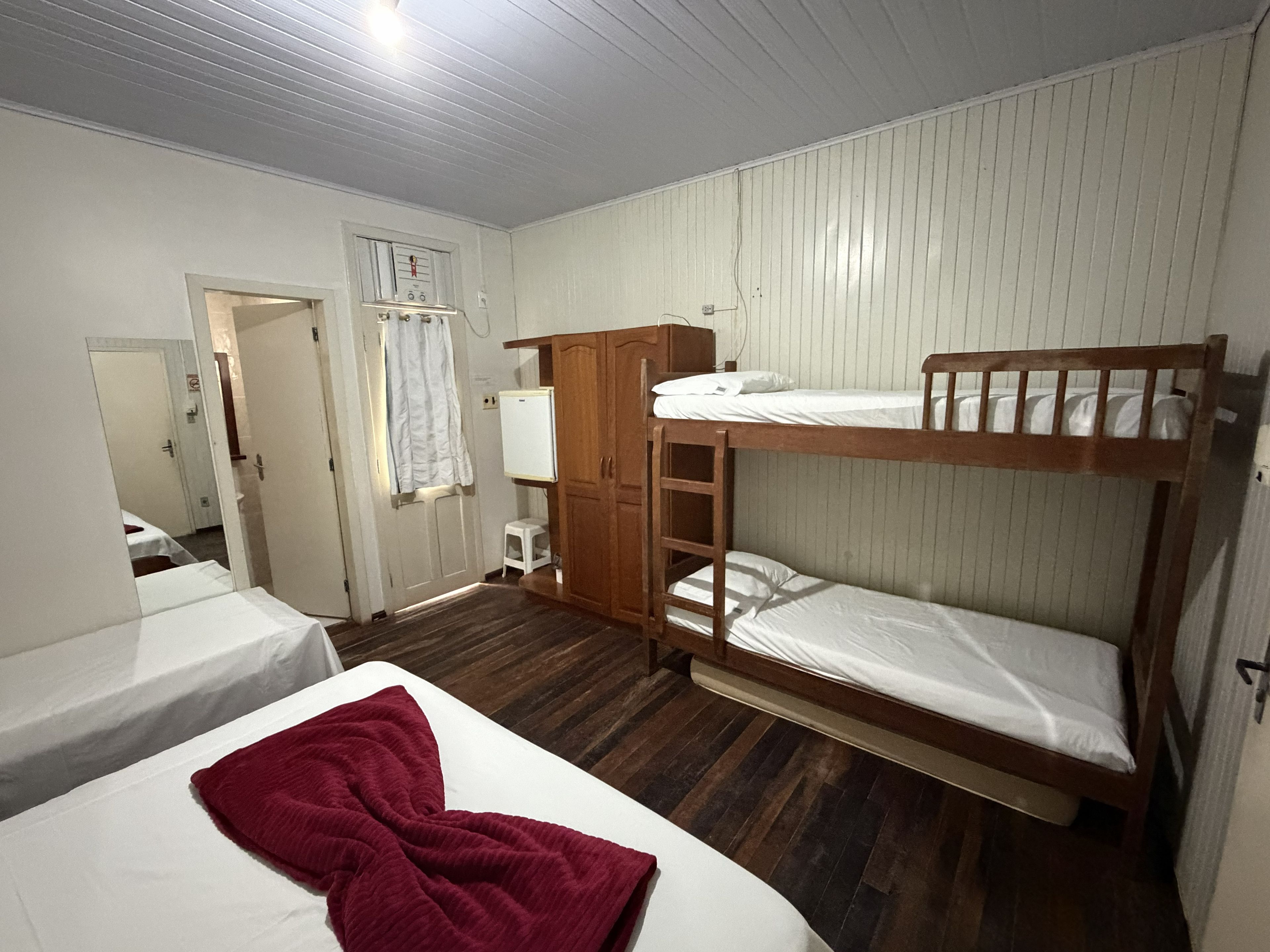Una habitación con literas, un armario de madera, un radiador blanco y una manta roja sobre una de las camas.