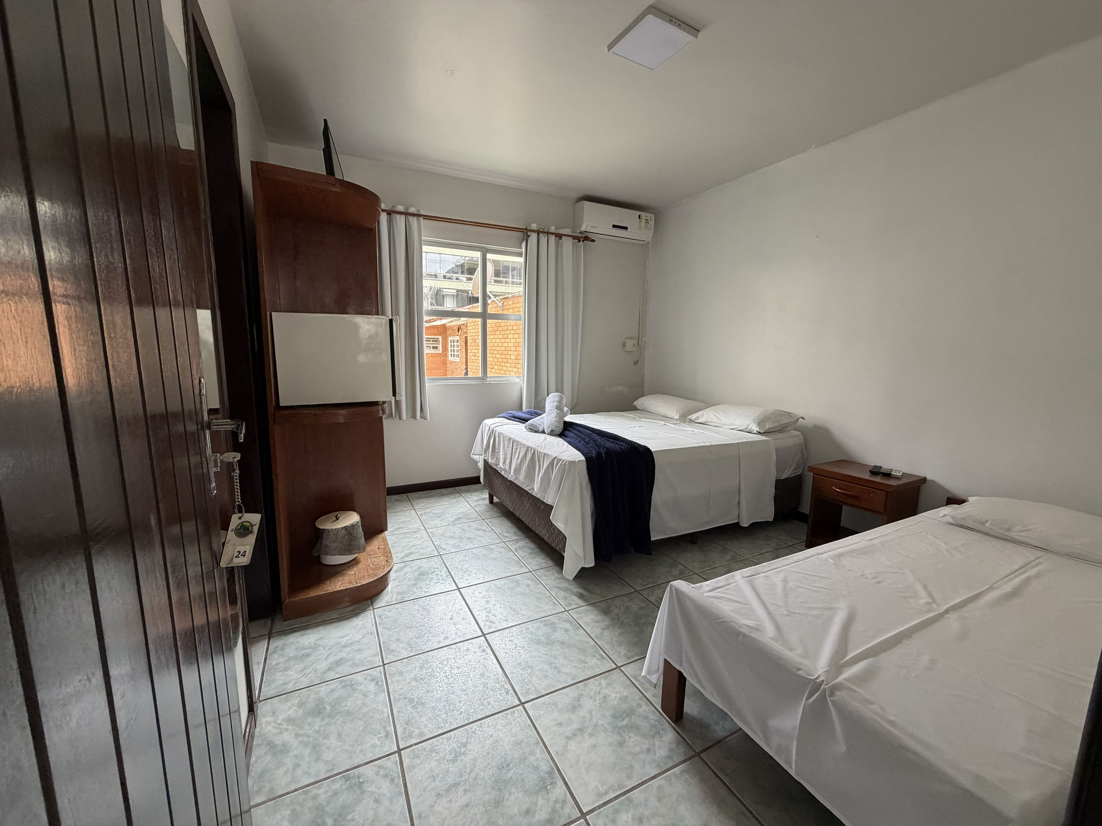 A hotel room with a bed, a desk, a wardrobe, a window, and a ceiling light.