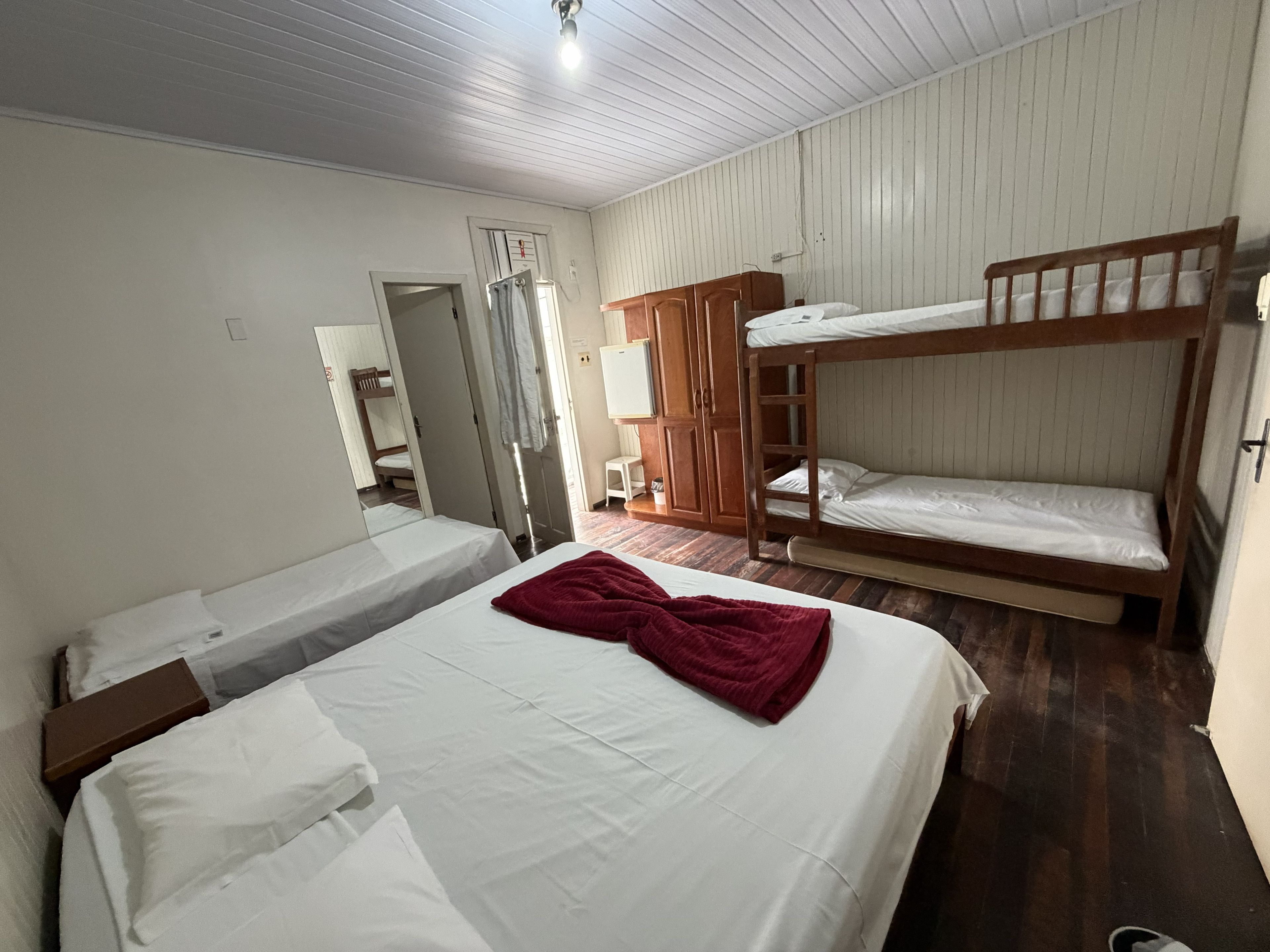 Una habitación con dos camas individuales, una litera, un armario de madera y un espejo.