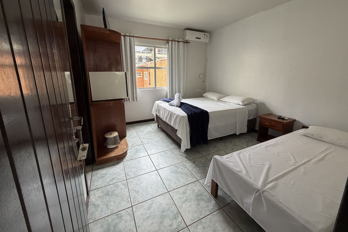 Ett hotellrum med en säng, ett skrivbord, en garderob, ett fönster och en luftkonditioneringsanläggning.