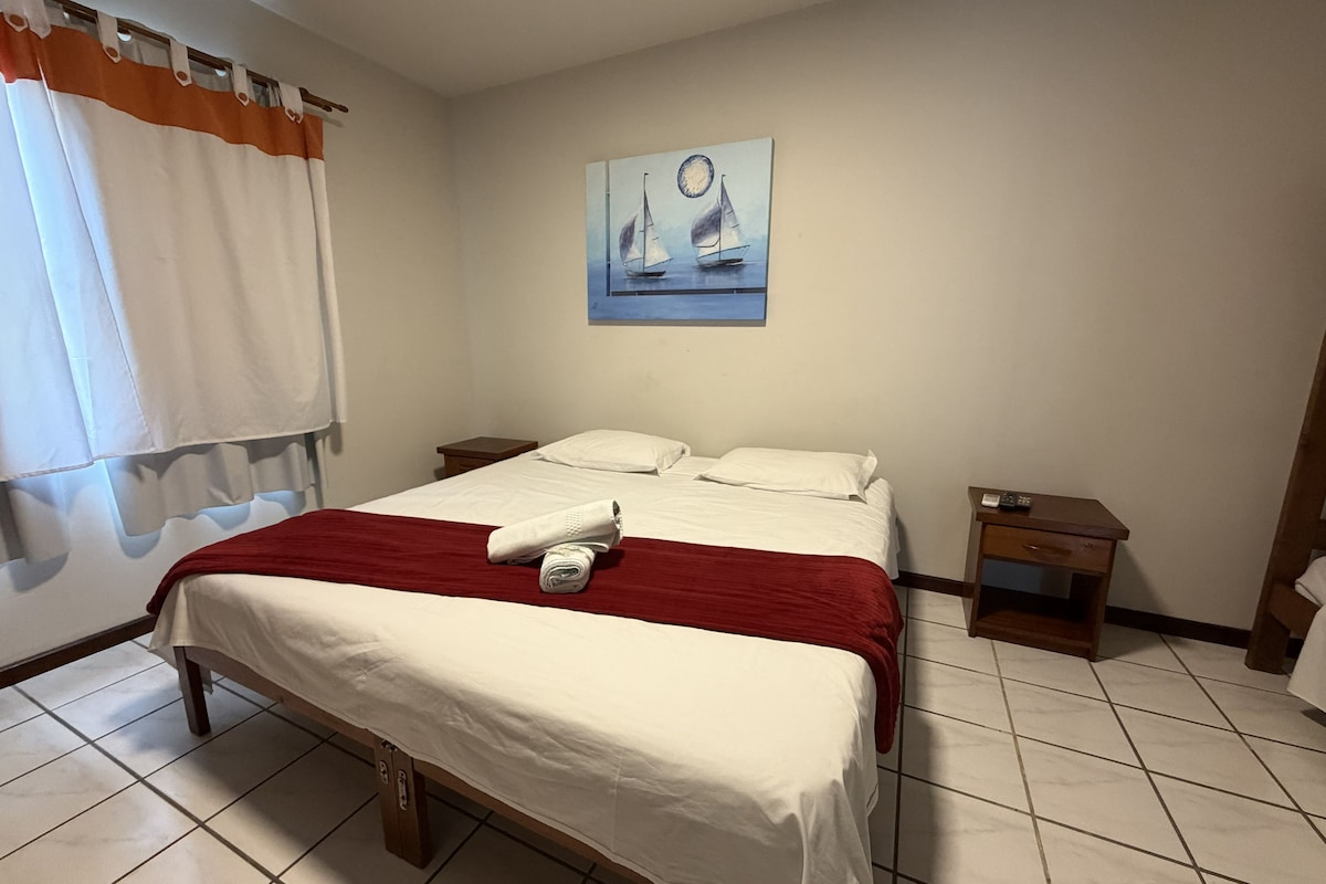 Ett hotellrum med en säng, ett nattduksbord, en tavla och ett fönster med gardiner.