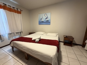 Habitació d'hotel amb un llit, una taula de nit, un quadre i una finestra amb cortines.