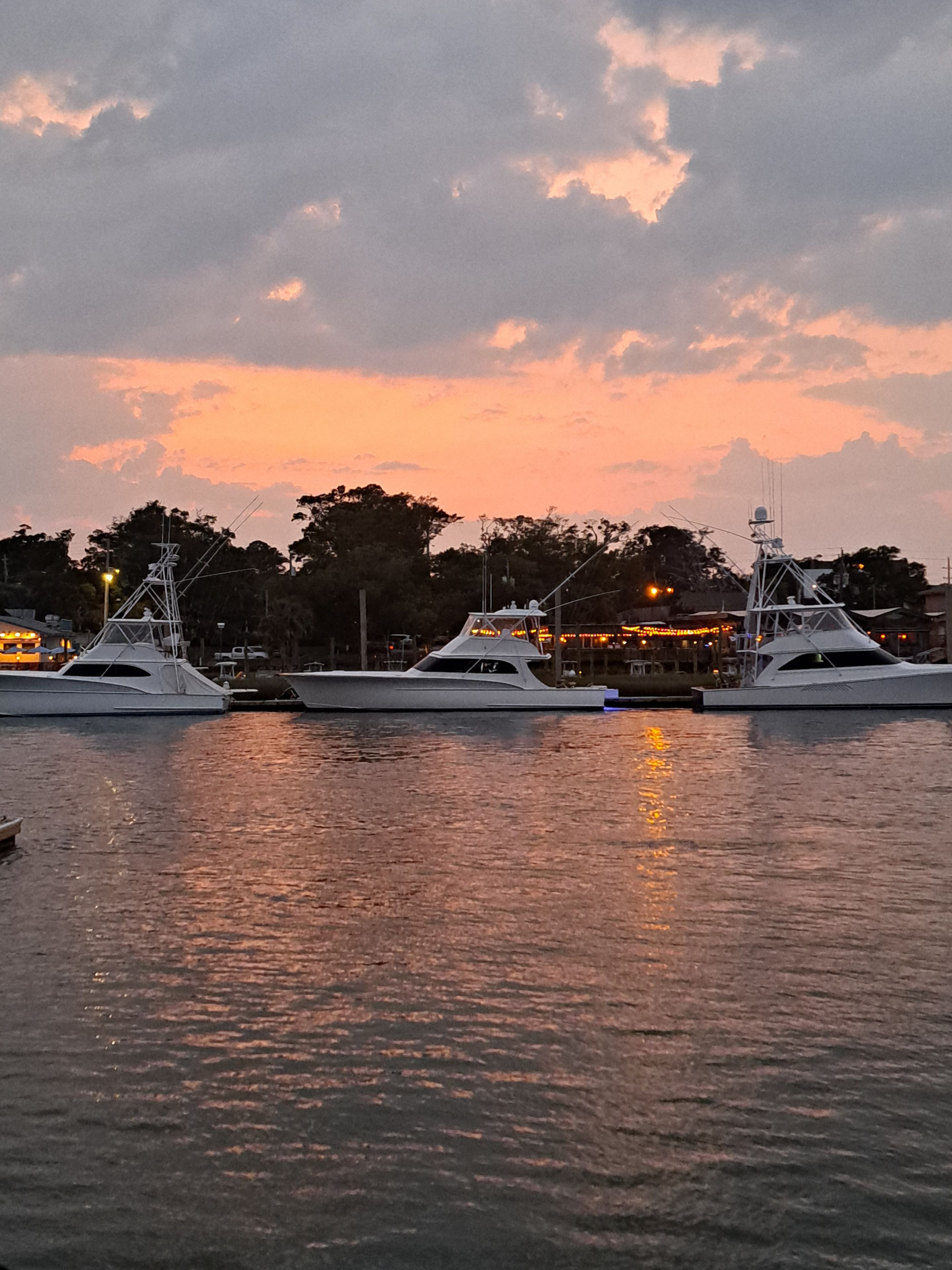 Un puerto deportivo con varios yates amarrados, agua tranquila y un cielo al atardecer.