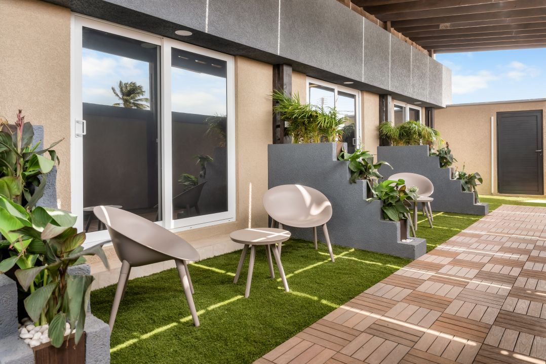 A modern outdoor patio with a herringbone tile floor, a small round table, two lounge chairs, and potted plants.