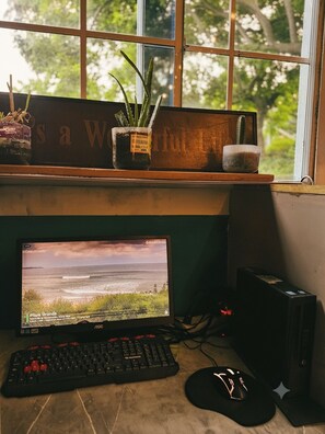 Un escritorio con monitor, teclado y ratón, una planta pequeña y un cartel decorativo.