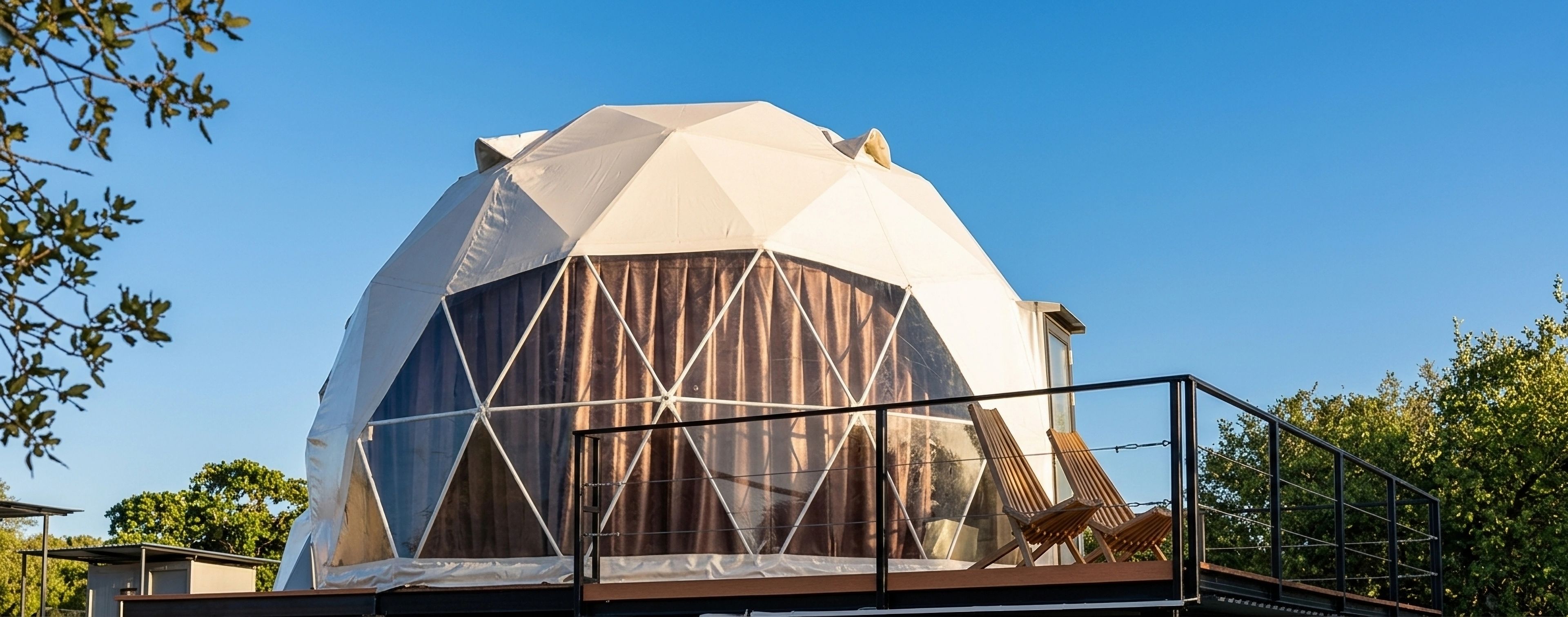Een geodetische koepelstructuur met een overdekte ingang en een balkon met stoelen.