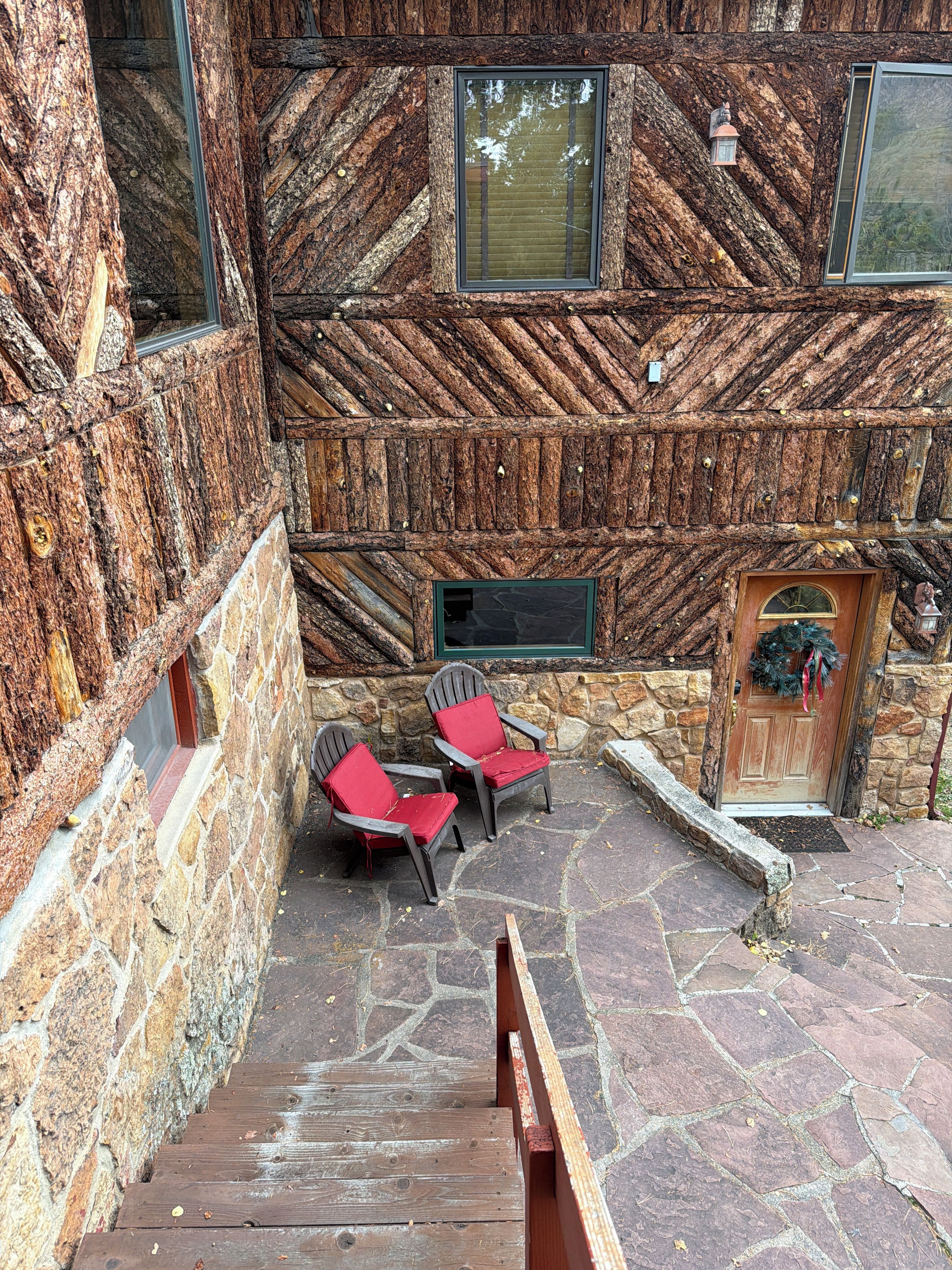 A stone building with a wooden exterior, a wooden staircase, and two red chairs outside.