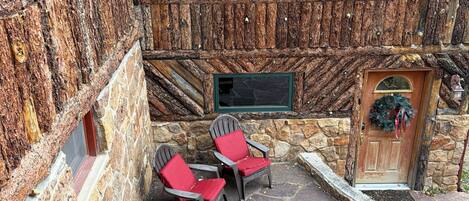 A stone building with a wooden exterior, a wooden staircase, and two red chairs outside.