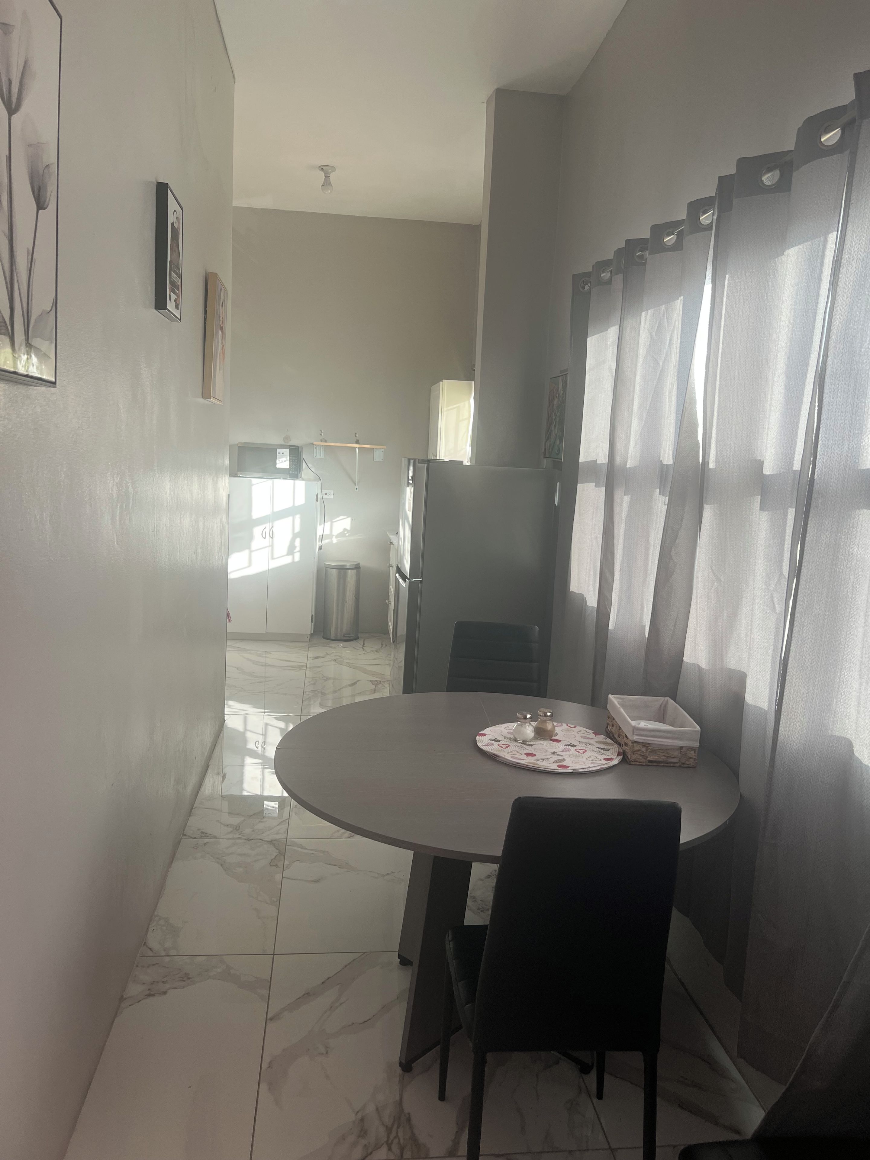 A dining area with a marble floor, a round table with chairs, and a window with curtains.