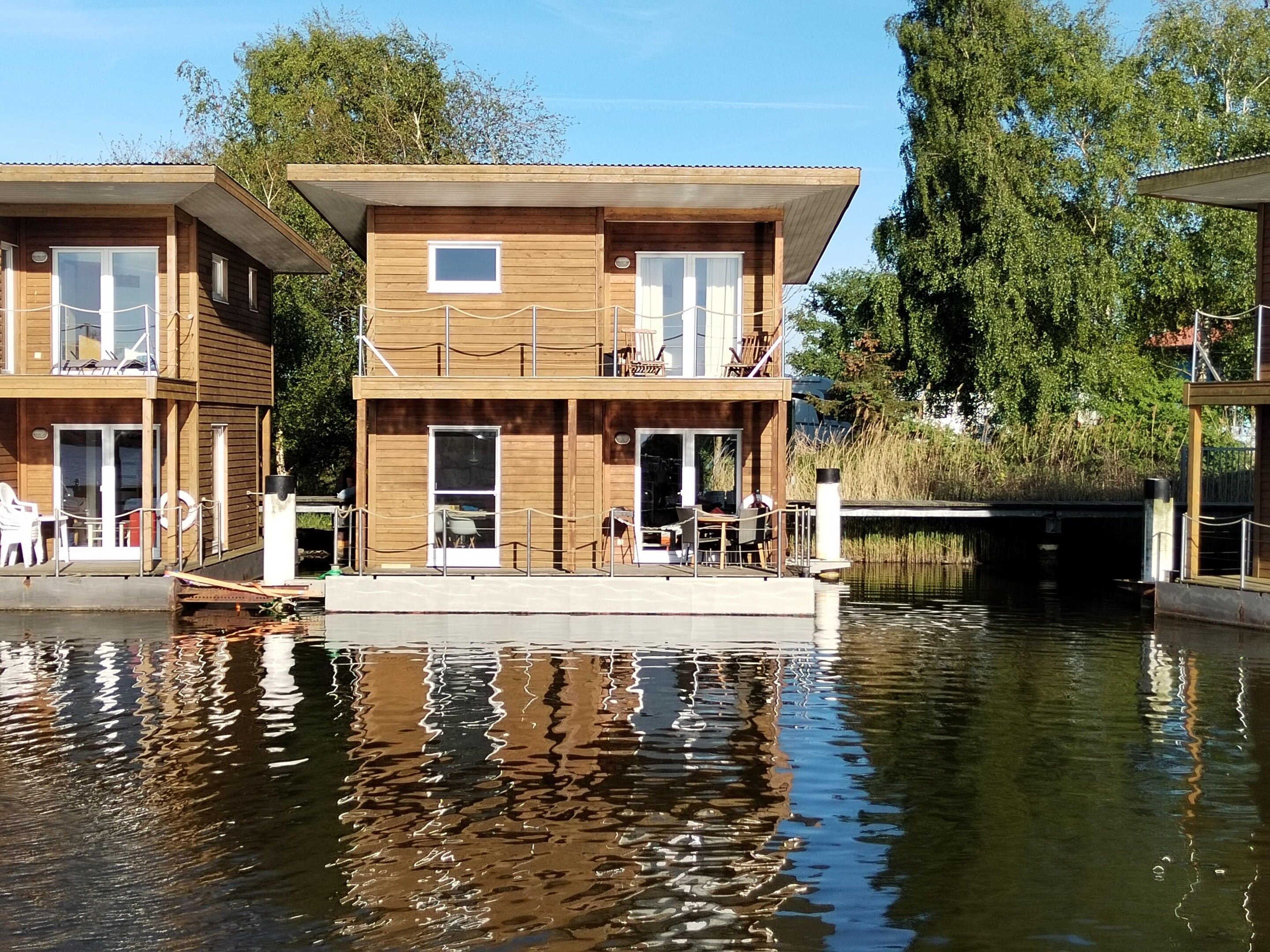 A wooden floating house with a balcony, a dining area, and a small pool.
