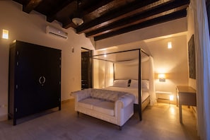 Un dormitori amb un llit amb cortines, un sofà, un armari i una tauleta de nit amb una làmpada.