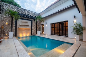 A swimming pool with a stone wall and a pergola, surrounded by potted plants. - Luxury 7 Bedroom Villa in Walled City (Cartagena de Indias)