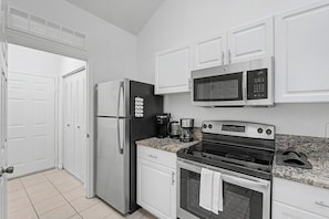 A compact kitchen with white cabinets, a stainless steel refrigerator, a microwave, a coffee maker, and an oven. - Cozy Gainesville Apt • 2BR 2BA Stay near UF Campus (Gainesville)