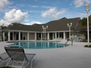 En swimmingpool med solstolar, en överbyggd paviljong och en byggnad med ett sluttande tak.