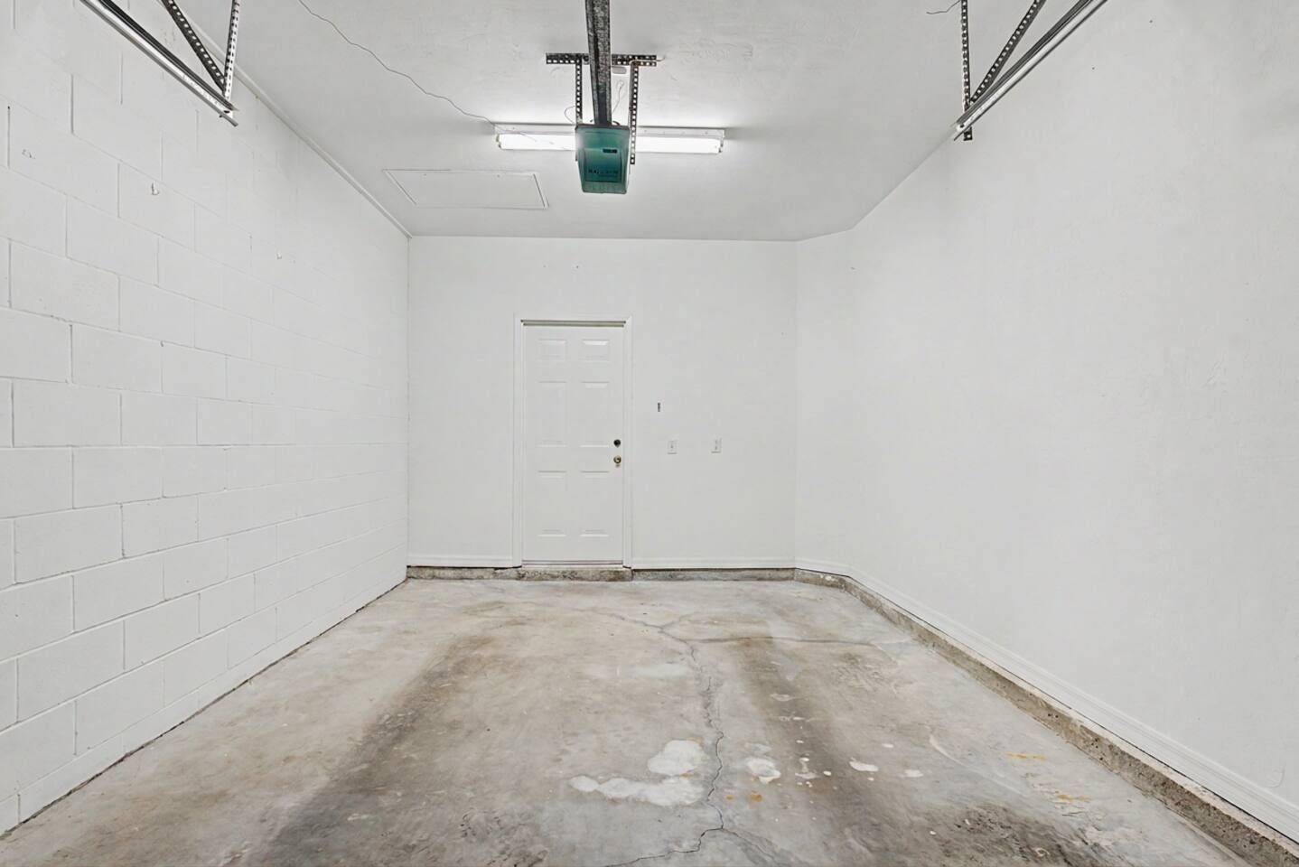 A room with white brick walls, a concrete floor, a door, and a ceiling light fixture.