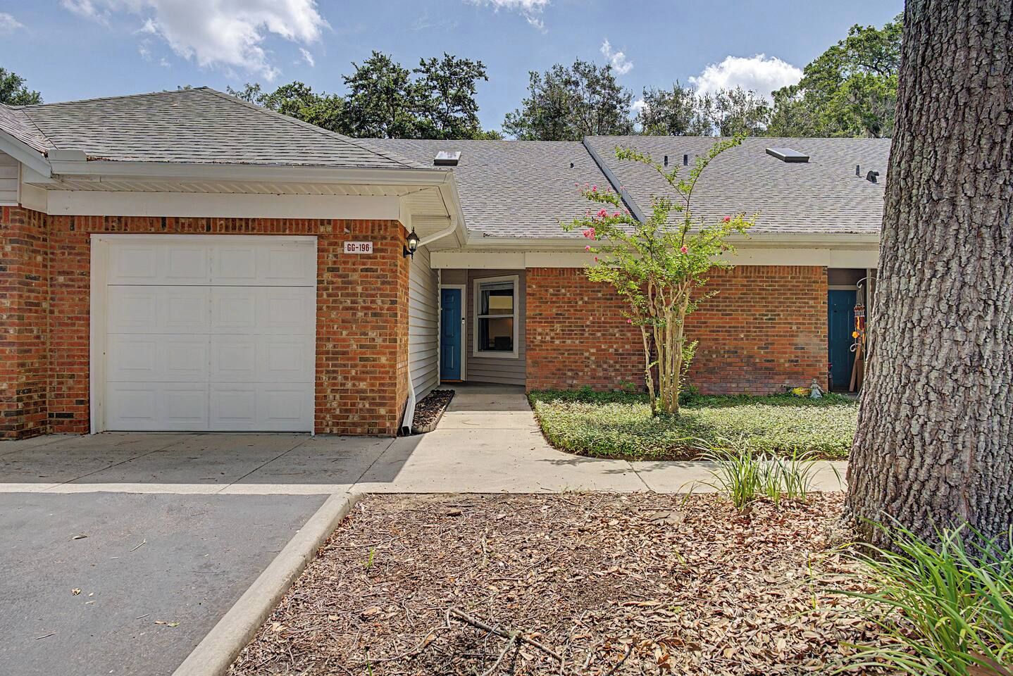 A two-story building with a garage, a small tree in the front yard, and a tree to the right.