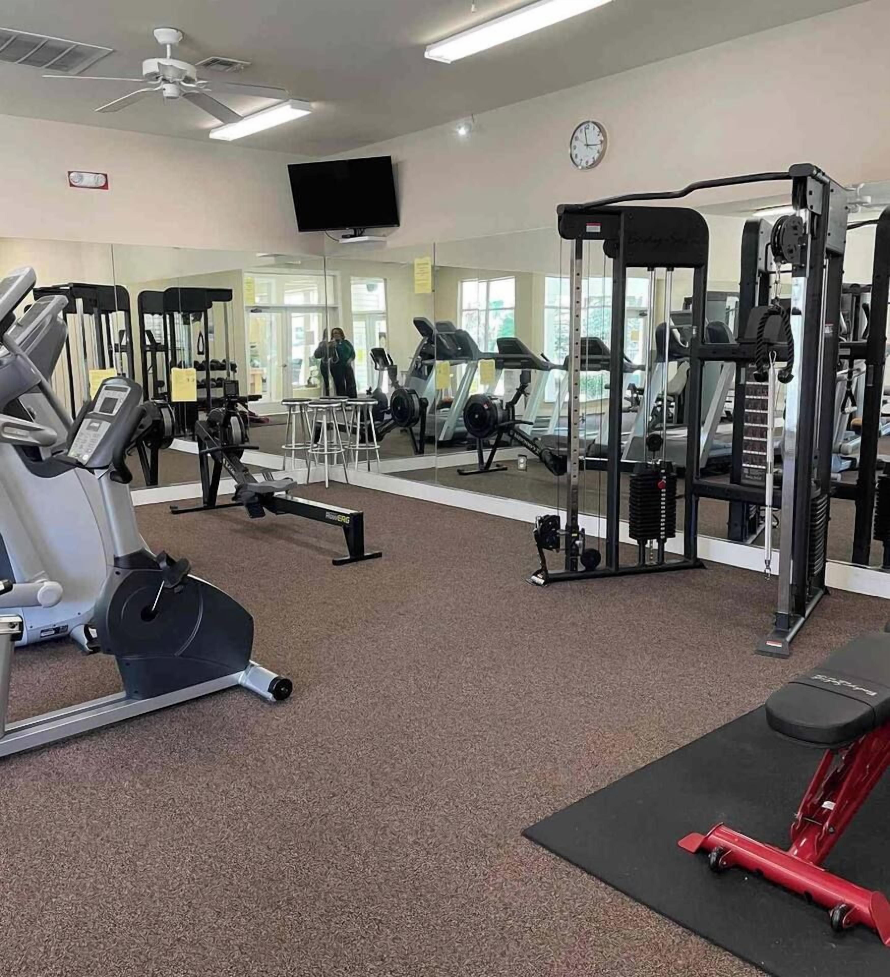 Une salle de sport équipée de divers appareils d’exercice, avec un téléviseur accroché au mur et une horloge.