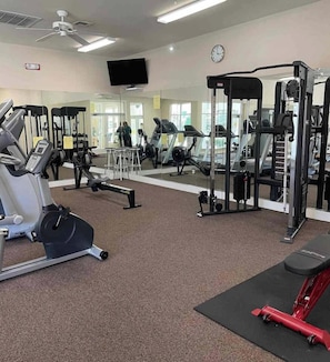 A gym with various exercise equipment, a television on the wall, and a clock. - Cozy Gainesville Apt • 2BR 2BA Stay near UF Campus (Gainesville)