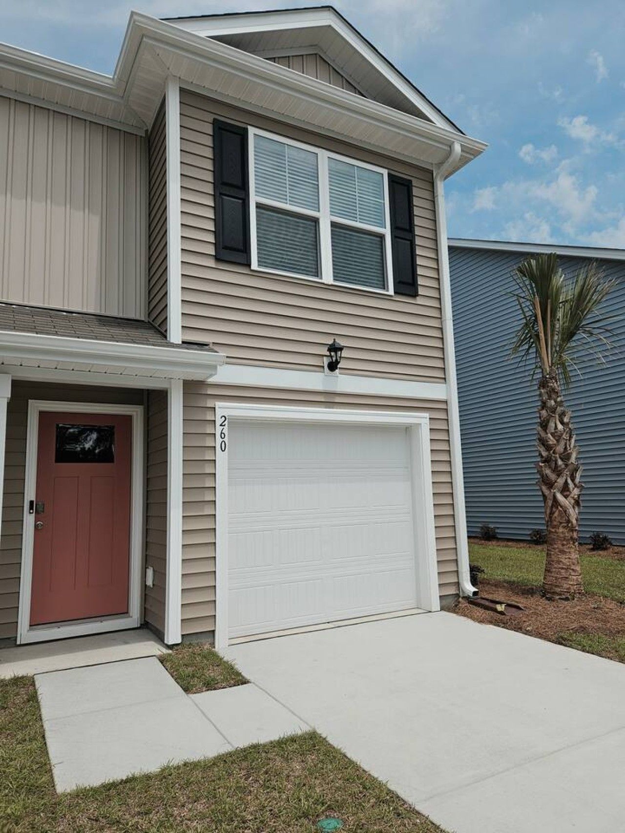 Une maison à deux étages avec un garage, une porte rouge et un palmier dans la cour.