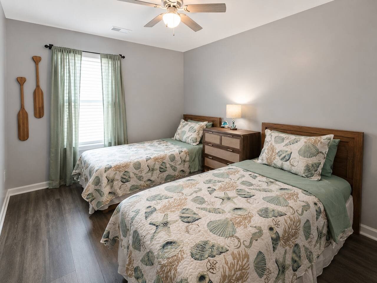 Une chambre avec deux lits, un ventilateur de plafond, une table de chevet avec une lampe et une fenêtre avec des rideaux.