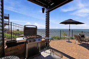 Une terrasse extérieure équipée d’un barbecue, d’une chaise pliante et d’un parasol.