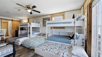 A bunk bed room with a ceiling fan, wooden walls, and a window.