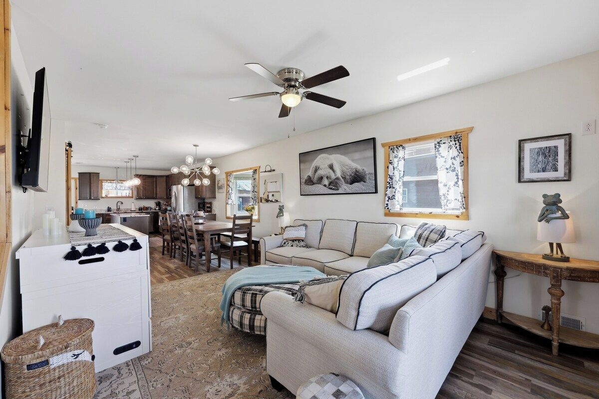 Un salon avec un canapé, un téléviseur, un ventilateur de plafond et une cuisine à l’arrière-plan.
