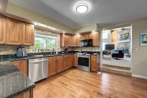 A modern kitchen with wooden cabinets, stainless steel appliances, and a stone backsplash. - Lighthouse Landing - 600 ft of Private Beach Views (Vermilion)