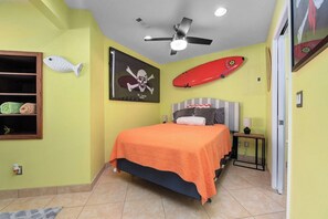 A bedroom with a bed, a ceiling fan, a fish decoration, a skull and crossbones poster, and a surfboard. - Captains Cove: 600 Feet of Shared Private Beach (Vermilion)