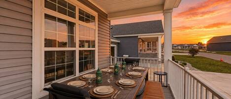An outdoor dining area with a table set for four, a covered porch, and a view of the sunset.