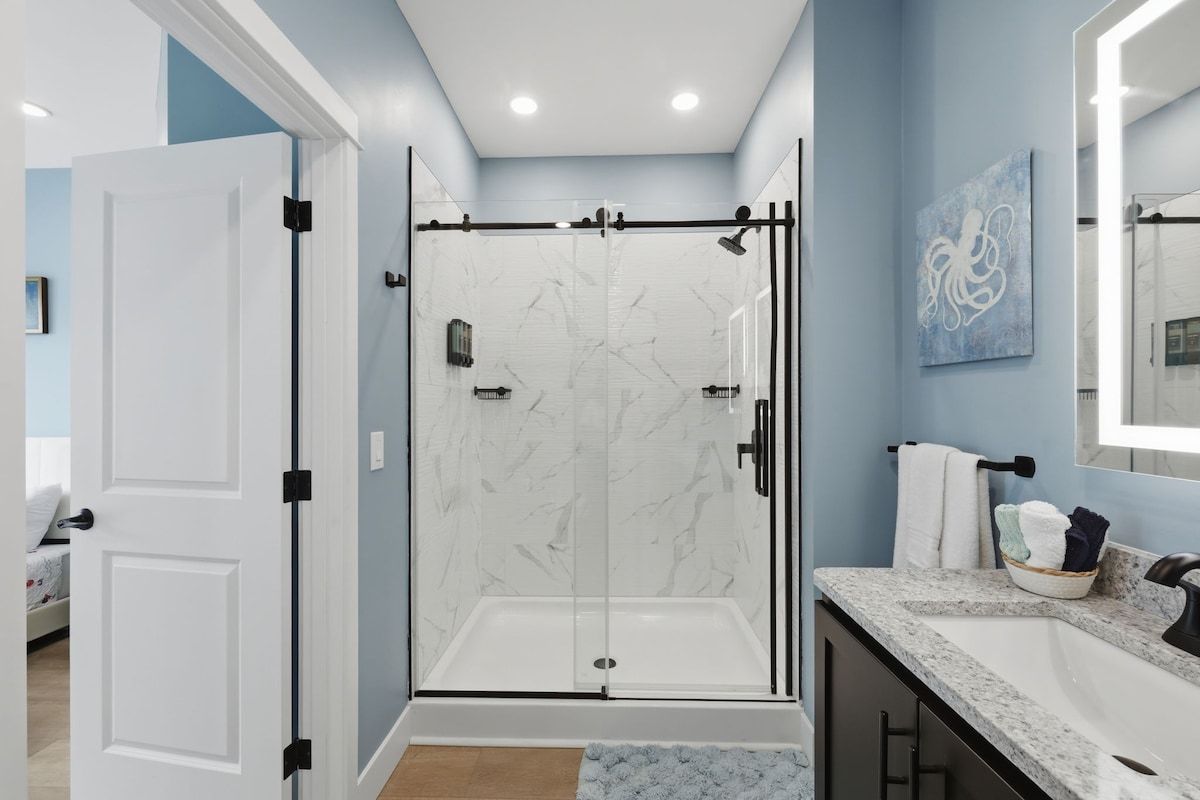 A modern bathroom with a glass-enclosed shower, a marble-tiled wall, and a sink with a marble countertop.