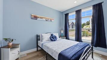 A bedroom with a bed, a nightstand, a window with curtains, and a wall-mounted picture.