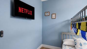 A room with a bed, a wall-mounted TV displaying 'NETFLIX', a framed picture, and a flag.