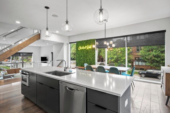A modern kitchen with a central island, stainless steel appliances, and a view of the outdoors through large windows. - Twin Terraces-Skyline Views with Two Rooftop Decks (Cleveland)