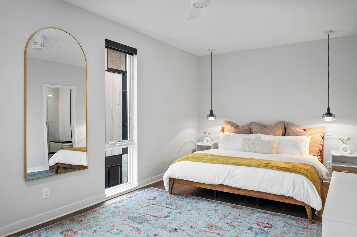 Une chambre à coucher avec un lit, un grand miroir, une fenêtre et deux lampes suspendues.