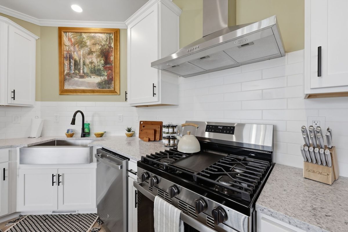 A modern kitchen with white cabinets, a stainless steel stove, and a painting on the wall.