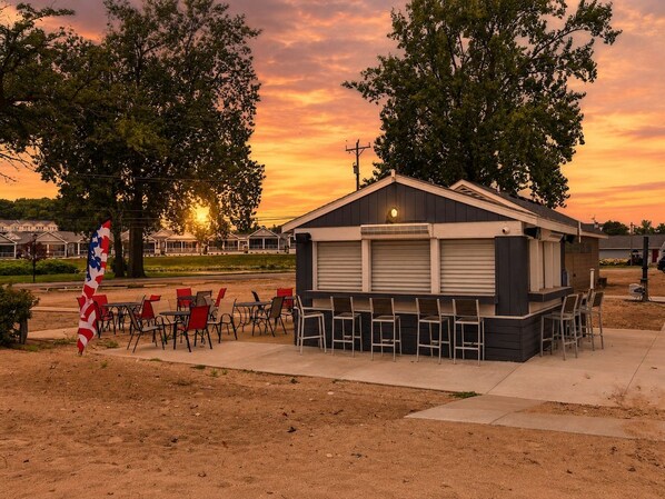 A small building with a closed shutter, surrounded by outdoor seating with chairs and tables. - Baypoint Bungalow-Pool, Beach, and Arcade (Lakeside Marblehead)
