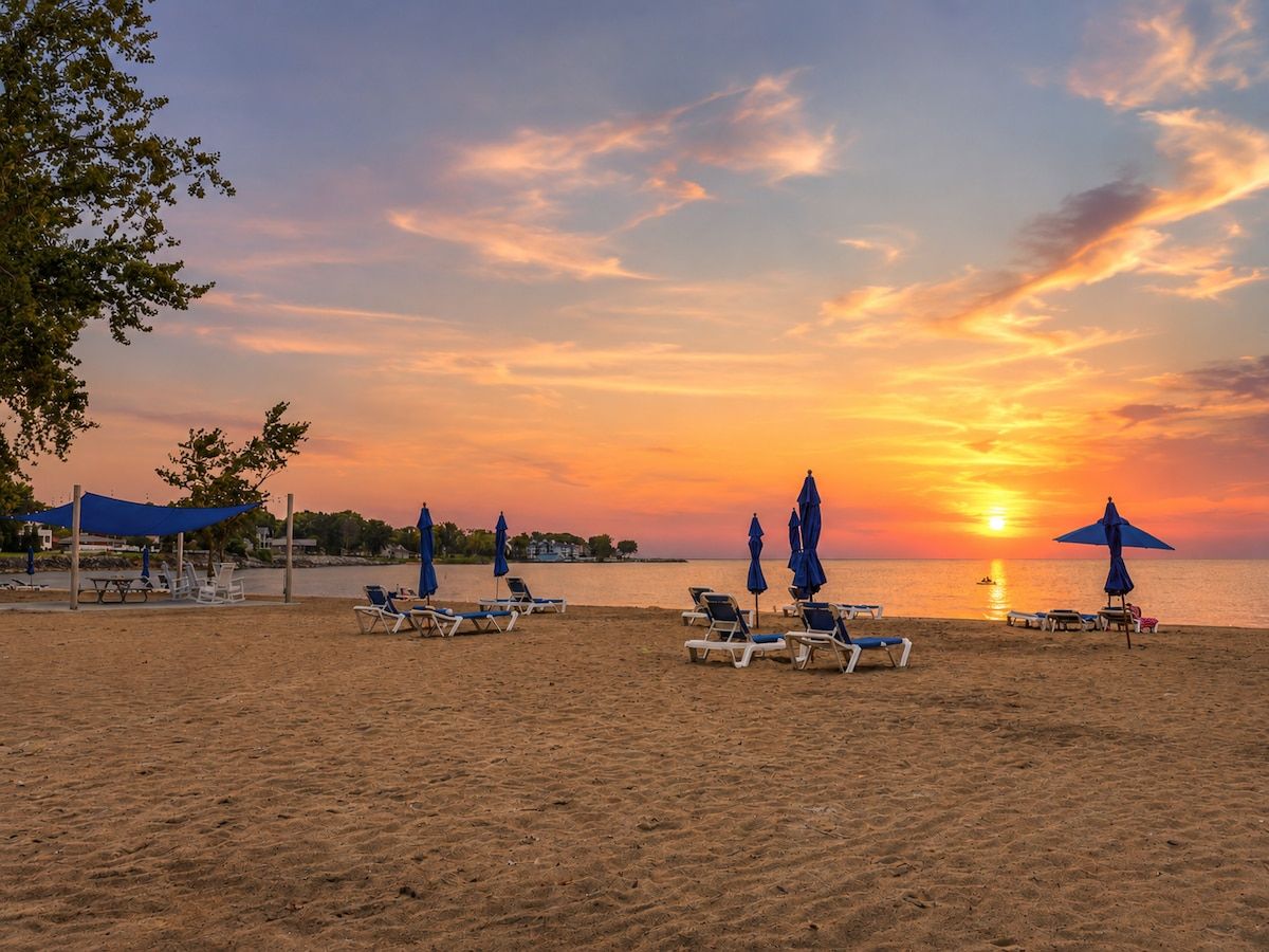 A beach with sun loungers and umbrellas, a clear sky, and a sunset over the water.