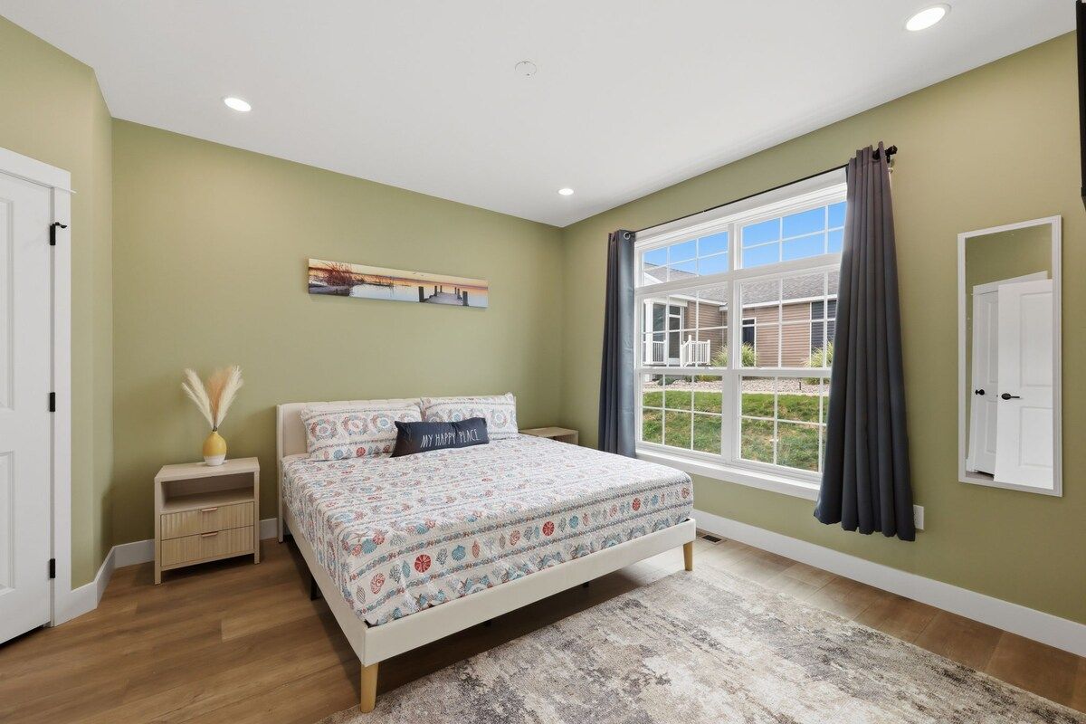 A bedroom with a bed, a nightstand, a window with curtains, and a door.