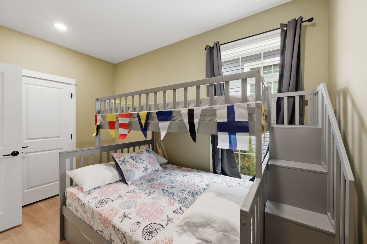 A bunk bed with a white headboard, a window with curtains, and a door.
