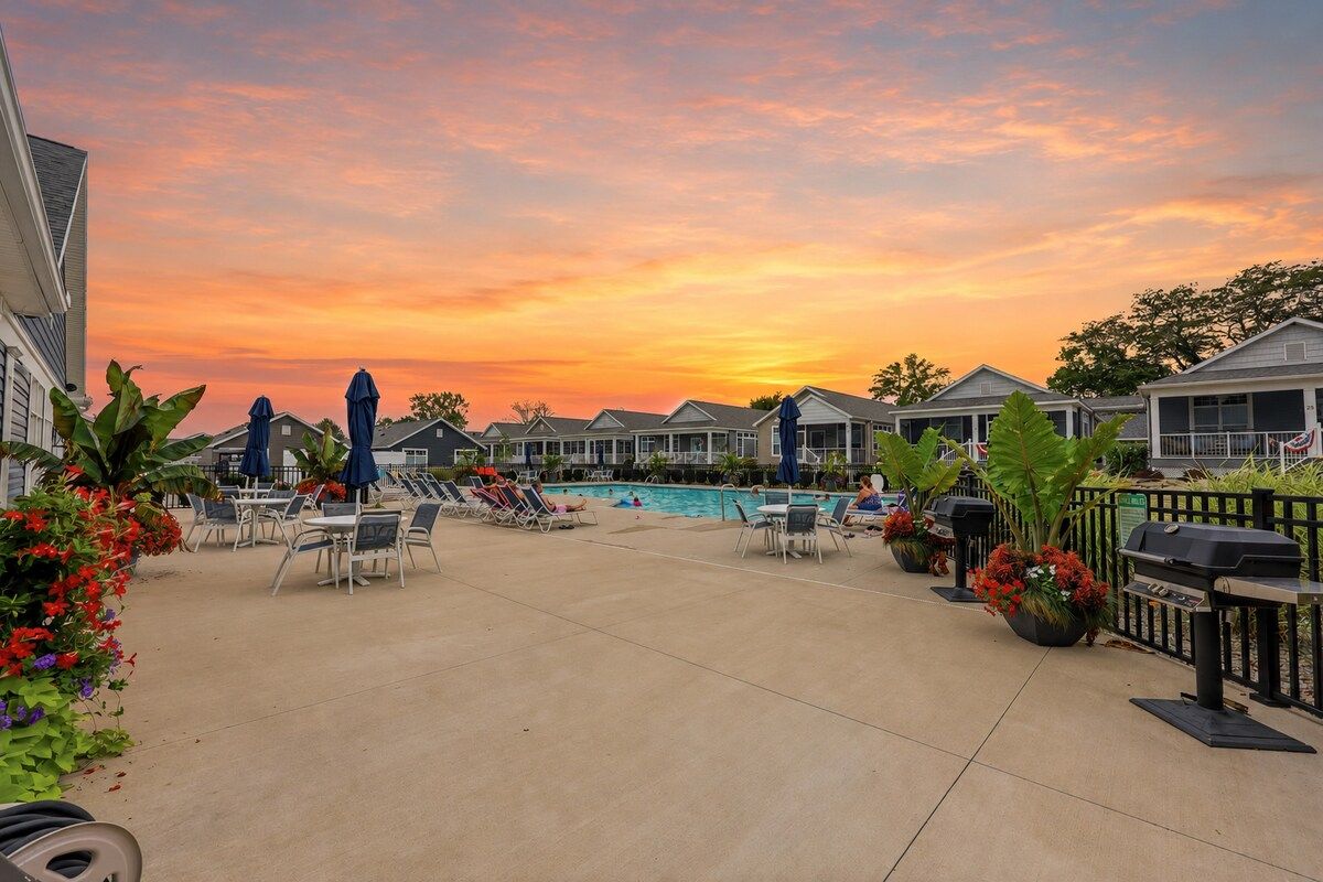 A poolside area with lounge chairs and umbrellas, surrounded by buildings with a view of the sunset.