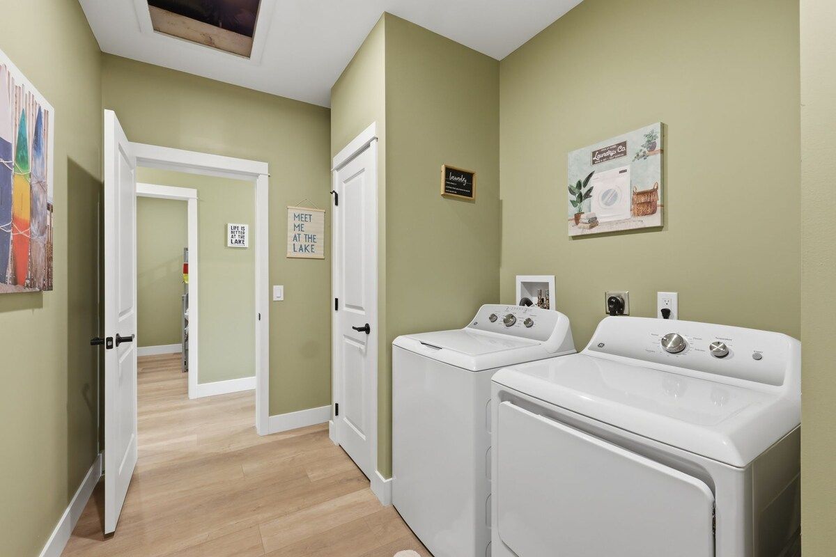 A laundry room with two white washing machines, a door leading to another room, and a sign on the wall.