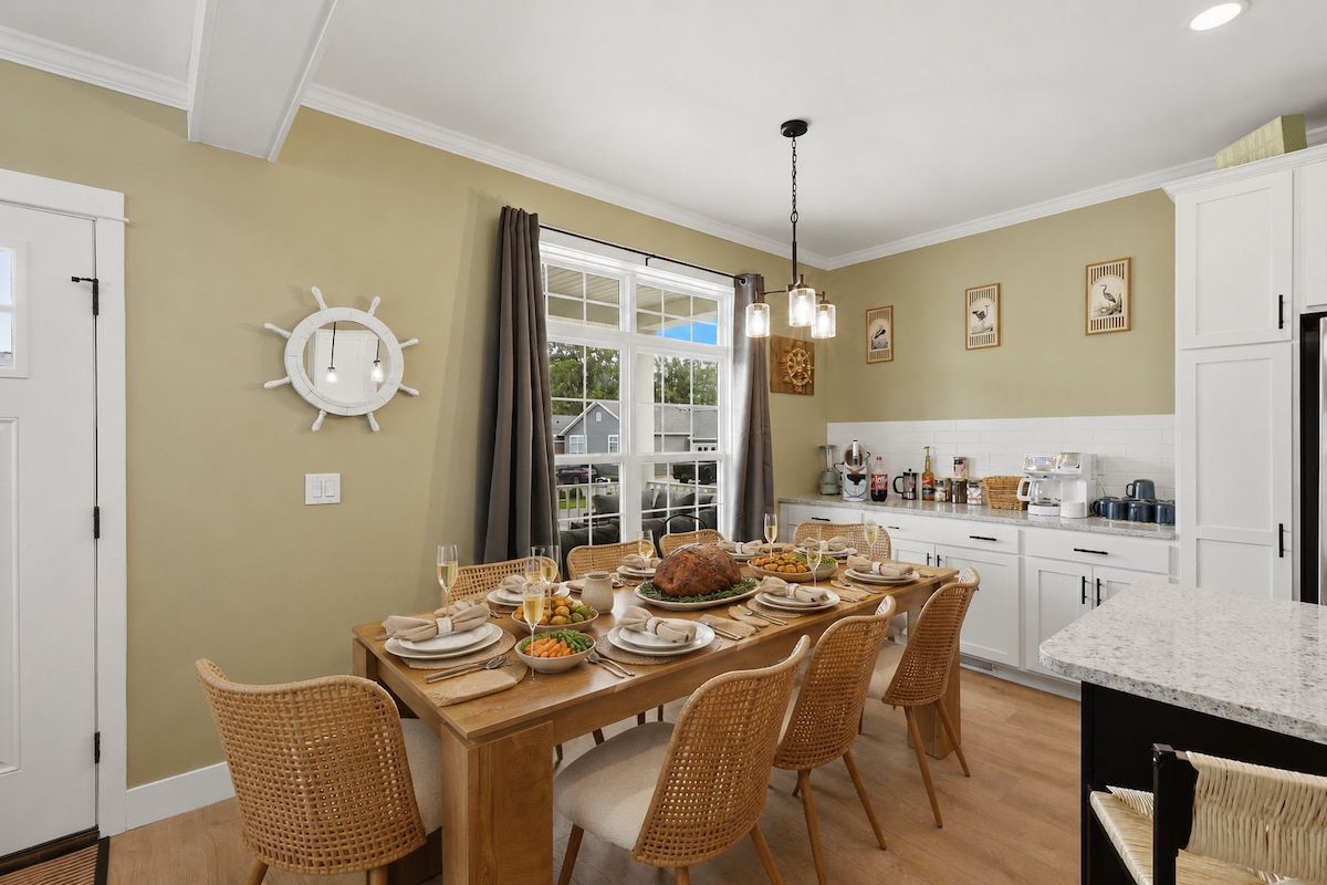 A dining area with a long table set for a meal, surrounded by wicker chairs.