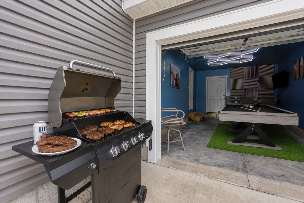 A barbecue grill with food, a pool table, and a door leading to a room with a blue wall and a ceiling light fixture.