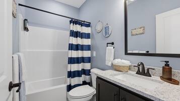 A bathroom with a bathtub, a toilet, a sink with a mirror, and a shower curtain.